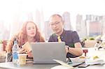 Businessman and woman looking at laptop at waterfront cafe with New York skyline, USA