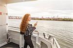 Young businesswoman on ferry deck looking at smartphone, New York, USA