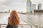 Rear view of long red haired businesswoman on ferry deck looking out at skyline, New York, USA