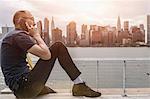 Businessman sitting on waterfront making smartphone call, New York, USA