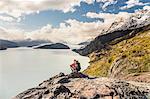 Male hiker crouching to look out over Grey Lake and Glacier, Torres del Paine national park, Chile