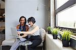 Two women sitting, working on laptop, on laptop stand