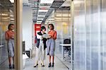Two businesswomen in office corridor, looking at digital tablet