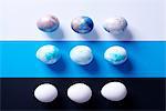 Overhead view of nine dyed easter eggs on blue, black and white striped background