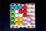 Overhead view of multi- coloured painted eggs in tray on black background