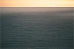 View from the land over the ocean, to the horizon at dusk. Light orange coloured sky and dark water.