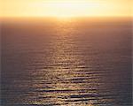 View from the land over the ocean, to the horizon. The sun resting on the horizon and light reflecting off the water.