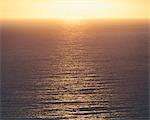 View from the land over the ocean, to the horizon. The sun resting on the horizon and light reflecting off the water.