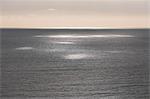 View from the land over the ocean, to the horizon. Sunlight patches on the water surface.