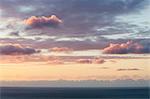 View from the land over the ocean, to the horizon. Sunset light shining on the clouds.