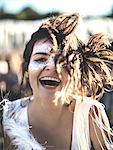 Young woman with long brown hair at a summer music festival face painted, smiling at camera.