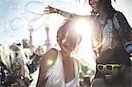 Revellers at a summer music festival young man wearing yellow sunglasses carrying woman on his shoulders.