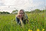 Portrait of blond woman lying on her front on a meadow, hand on chin, smiling at camera.