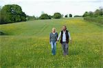 Man and woman walking hand in hand across a meadow.