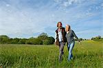 Man and woman walking arm in arm across a meadow.