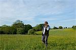 Man wearing sunglasses walking across meadow, holding mobile phone to his ear.