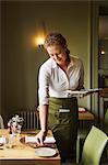 Woman wearing apron setting table in a restaurant.