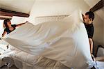 Man and woman standing in hotel room, making bed.