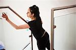 Woman standing on a staircase, cleaning a glass pane and banister rail.