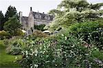 Exterior view of a 17th century country house from a garden with flower beds, shrubs and trees.