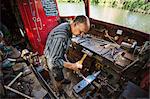 High angle view of blacksmith at his workbench on his working boat on the water, hammering hot metal.