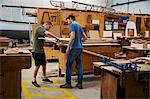 Two men standing at a workbench in a boat-builder's workshop, working on piece of wood.