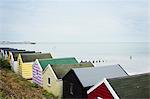 Row of colourful huts on a sandy beach under a cloudy sky.