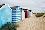 Row of colourful painted beach huts on a sandy beach under a cloudy sky.