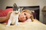 A woman lying on a bed stroking a small grey and white kitten