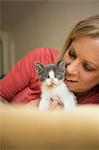 A woman stroking a small grey and white kitten.