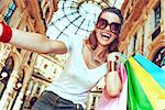 Discover most unexpected trends in Milan. Smiling fashion woman in eyeglasses with colorful shopping bags taking selfie in Galleria Vittorio Emanuele II
