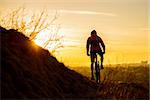 Silhouette of Enduro Cyclist Riding the Mountain Bike on the Rocky Trail at Sunset. Active Lifestyle Concept. Free Space for Text.