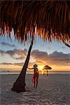 Bavaro Beach, Bavaro, Higuey, Punta Cana, Dominican Republic. Woman by thatch umbrellas on the beach at sunrise (MR).