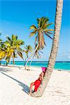 Canto de la Playa, Saona Island, East National Park (Parque Nacional del Este), Dominican Republic, Caribbean Sea. Beautiful woman with red sarong relaxing on the palm-fringed beach (MR).