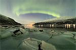 Northern Lights reflected in the cold sea frames the rocks covered with ice Manndalen Kafjord Lyngen Alps Tromsø Norway Europe