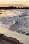 Silhouette of people walking along beach with pastel waves hitting shoreline at Byron Bay in New South Wales, Australia