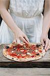 Woman putting ingredients on home-made pizza, mid section