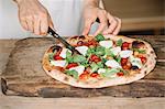 Woman cutting home-made pizza on chopping board, mid section