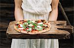 Woman holding home-made pizza on chopping board, mid section