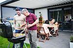 Mature and mid adult man barbecuing at family lunch on patio