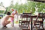 Senior and mature women dressing female toddler in pink bonnet at family lunch on patio