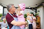 Mature man making faces at toddler granddaughter at family lunch on patio