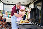 Female toddler barbecuing with grandfather at family lunch on patio