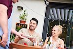 Man handing plate to couple with baby daughter at family lunch on patio