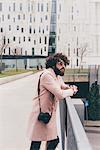 Young man standing on bridge, looking at view, camera over shoulder