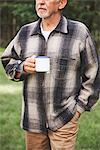 Senior man standing in rural setting, holding tin cup