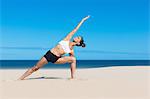 Woman on beach bending sideways arms raised in yoga position