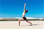 Side view of woman on beach arms raised stretching in yoga position