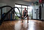 Man training with battle rope in gym