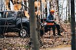 Male logger sitting on pick-up truck holding protective gloves in autumn forest